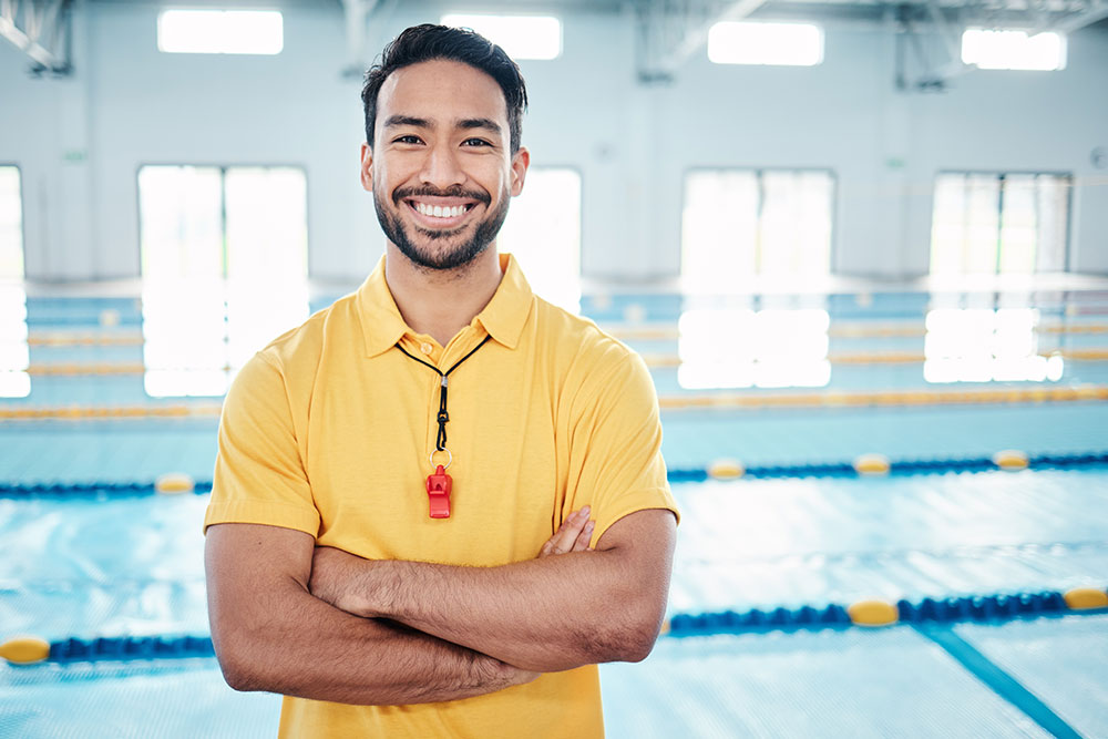 Coach smiling, standing in front of indoor pool